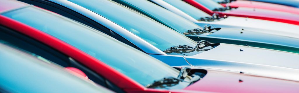 A row of parked cars in various colors lined up on a dealership lot
